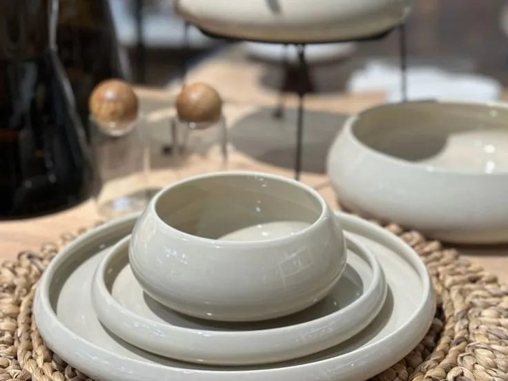 Assiettes et bol beige clair posés sur un set de table rond en fibres tressées