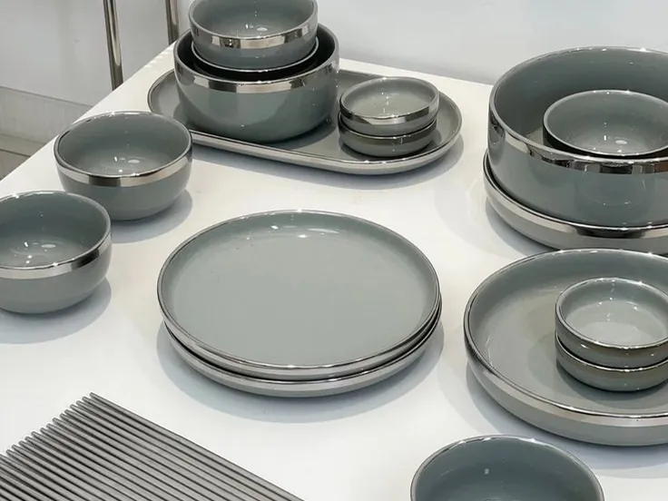 Assiettes et bols en grès gris à liseré argenté disposés sur une table blanche