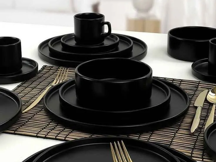 Vaisselle noire mate avec tasses et couverts dorés sur une table dressée
