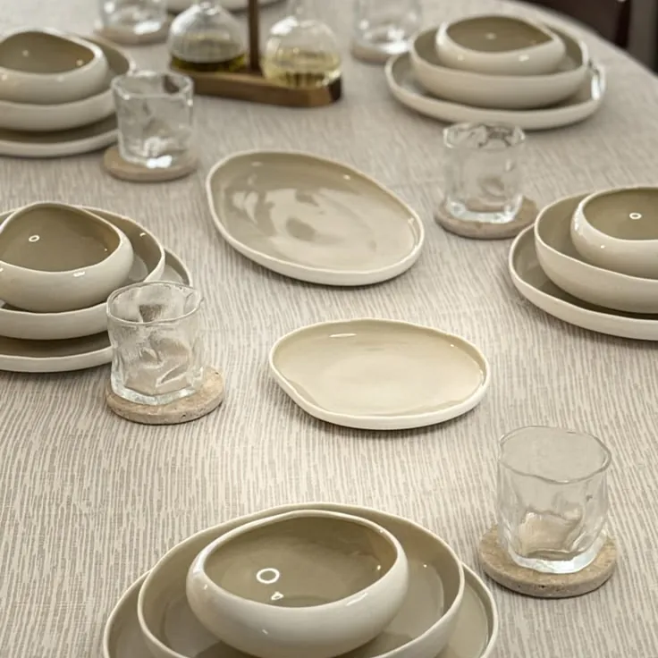 Table ronde nappée de lin dressée avec assiettes et bols beige et verres